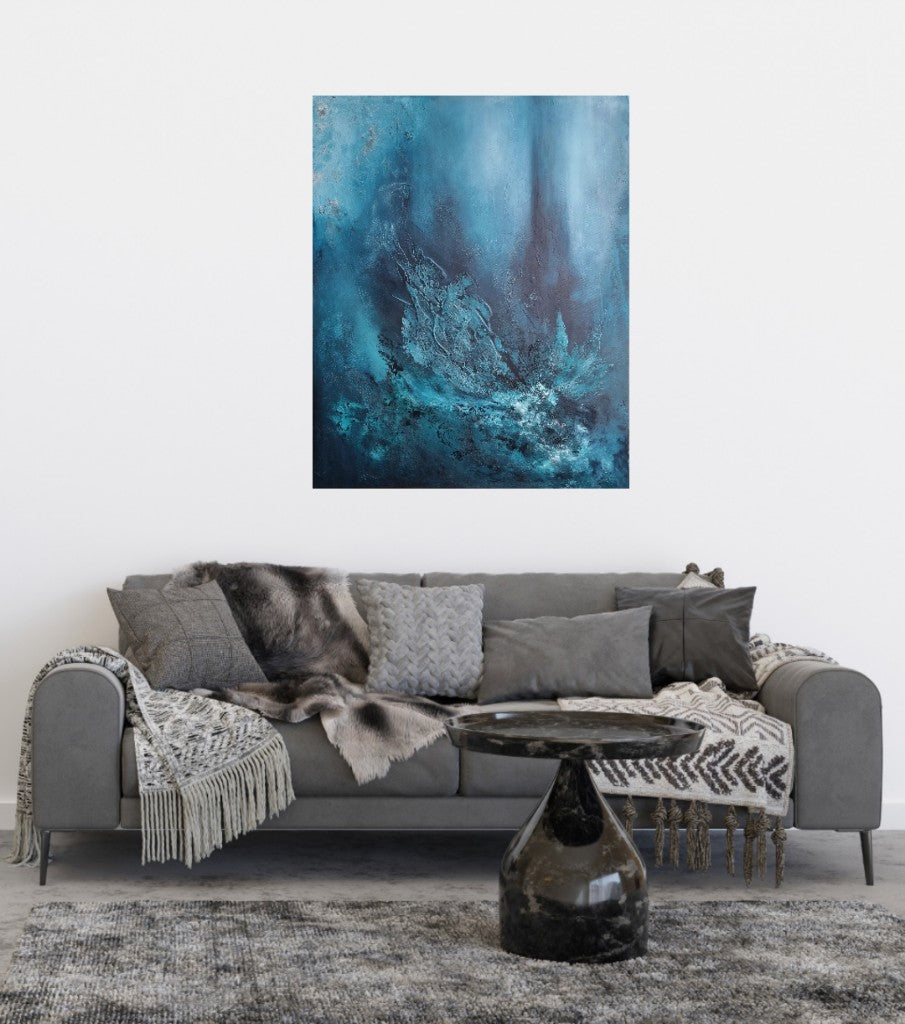 An abstract painting on a white wall above a gray sofa in a modern living room setting. The painting features various shades of blue with texture paste, created using acrylic paint on canvas. A rounded black coffee table and a gray rug complete the interior decor, giving a luxury look. 